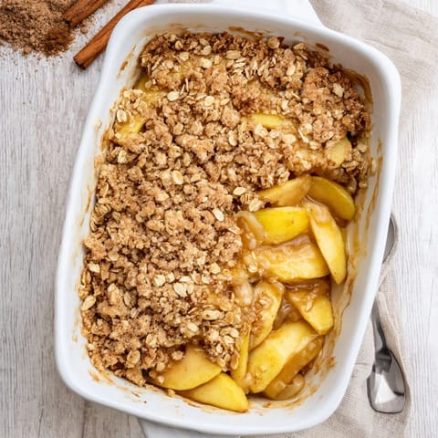 A scoop of vanilla ice cream slowly melts over warm Apple Crumble, served in a cozy ceramic bowl.