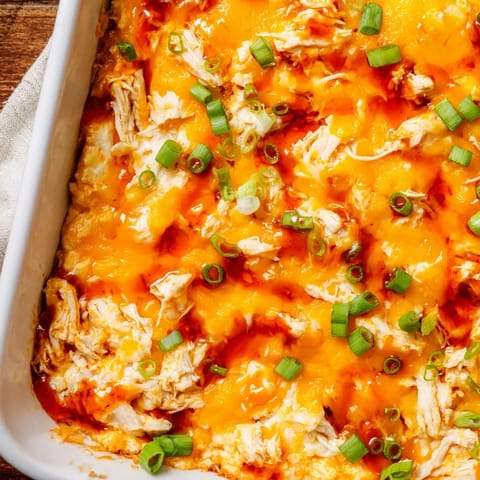 Spicy, creamy Buffalo Chicken Dip scooped from a dish onto a sturdy tortilla chip, with blue cheese crumbles and chives visible.