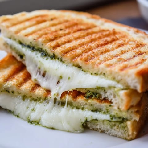 A warm Sourdough Pesto Grilled Cheese sandwich cut diagonally, showing gooey cheese pull and vibrant green pesto spread on thick bread.