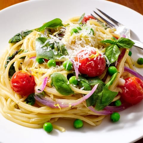 A vibrant Spring Veggie One-Pot Spaghetti topped with Parmesan and fresh basil, served hot from the pot.  