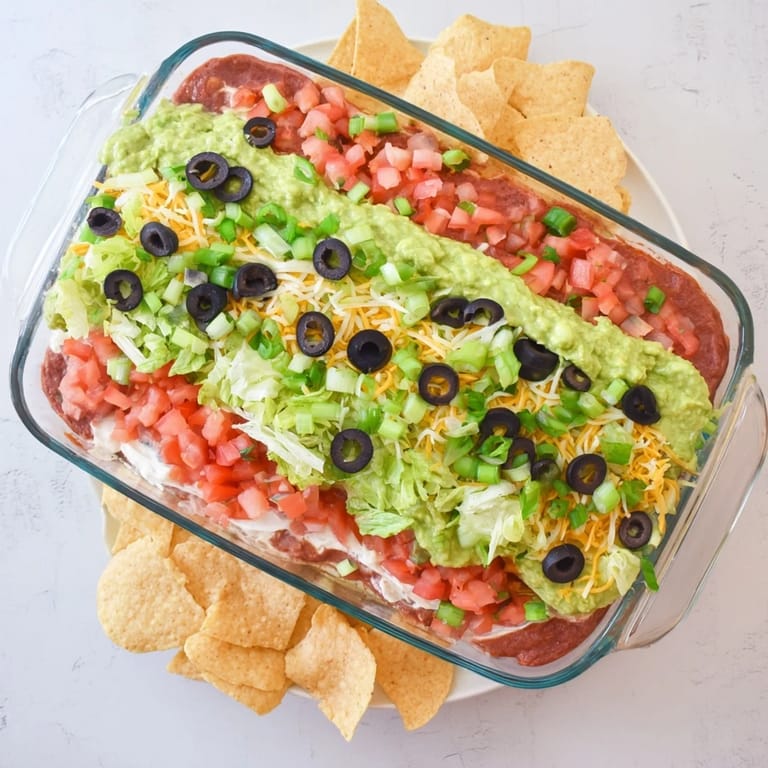Appetizer spread of seven-layer dip topped with lettuce and cheddar, surrounded by crunchy tortilla chips for dipping.