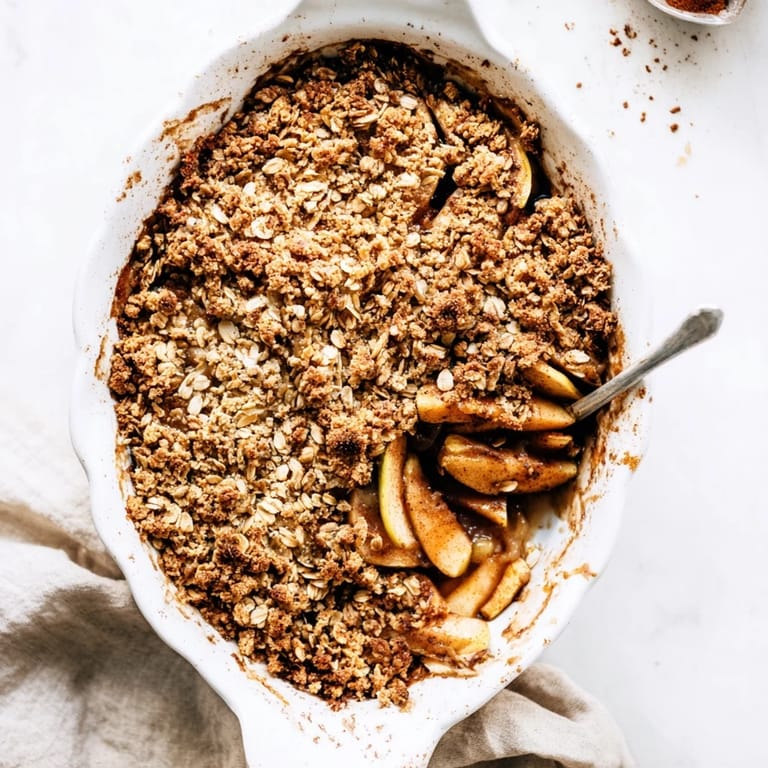 Rustic Apple Crumble features a golden-brown oat crumble topping, paired with a serving spoon and vanilla ice cream.