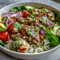 Vibrant pesto chicken bowl with fluffy rice, fresh cherry tomatoes, creamy avocado slices, and crisp cucumbers.